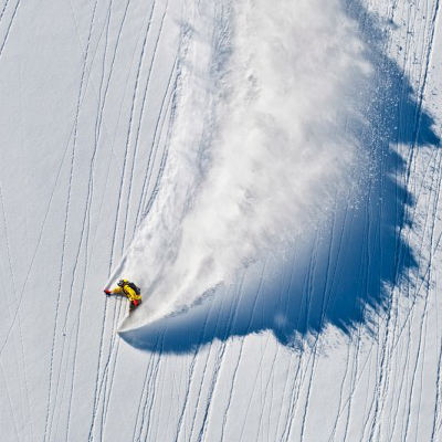 Skier descending mountain with large snow plume