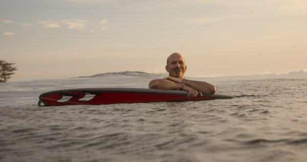Light skinned smiling man floating with a surfboard